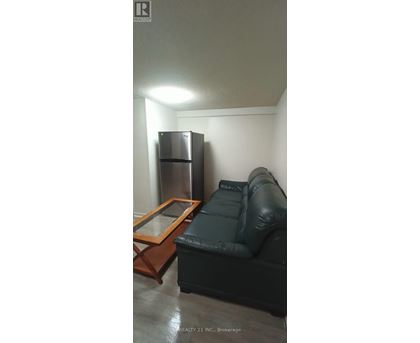 A black leather couch sits in a room with a wooden coffee table and a stainless steel refrigerator.
