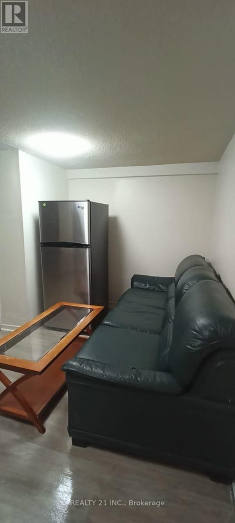A black leather couch sits in a room with a wooden coffee table and a stainless steel refrigerator.