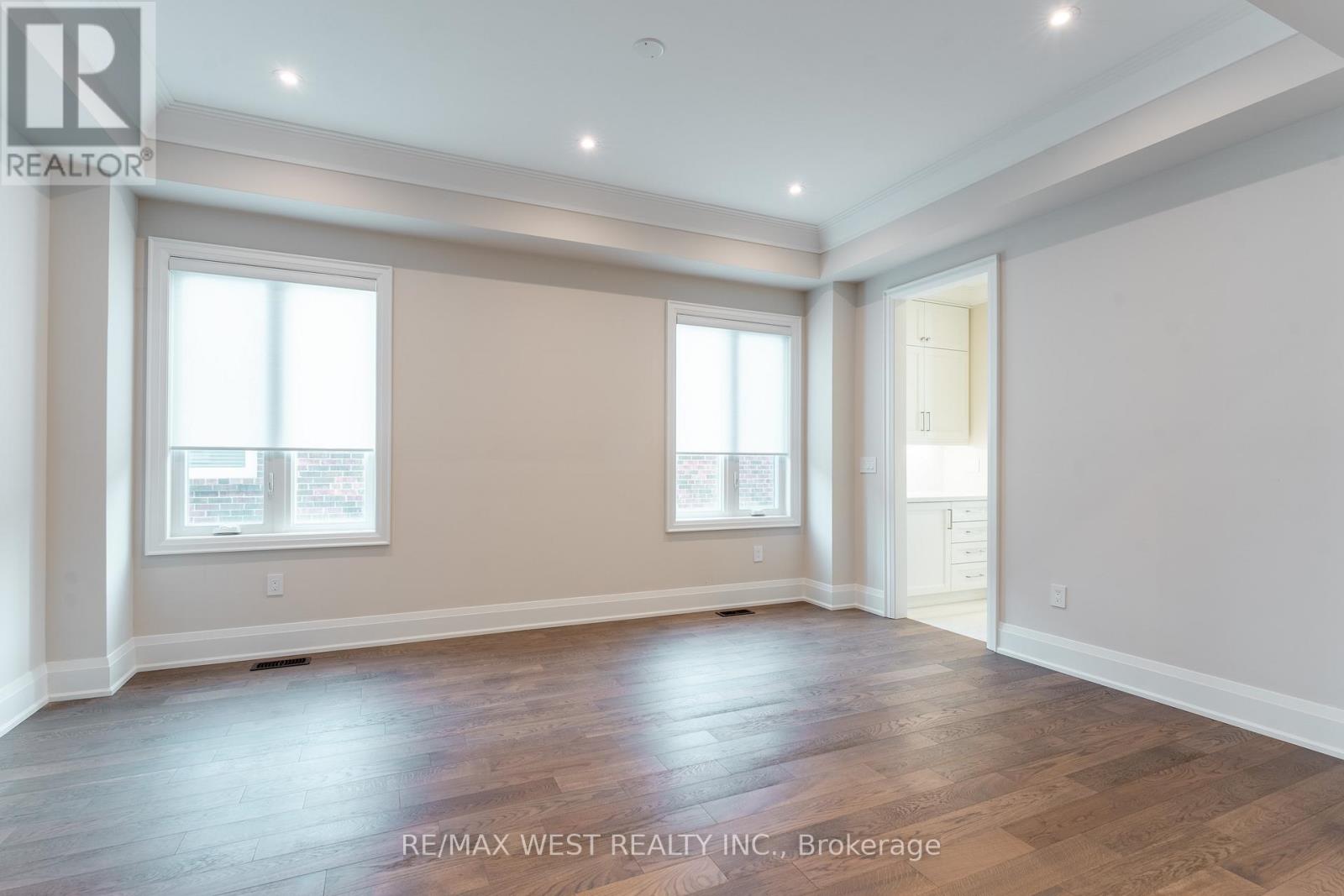 A spacious room with wooden flooring and two windows.
