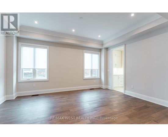 A spacious room with wooden flooring and two windows.