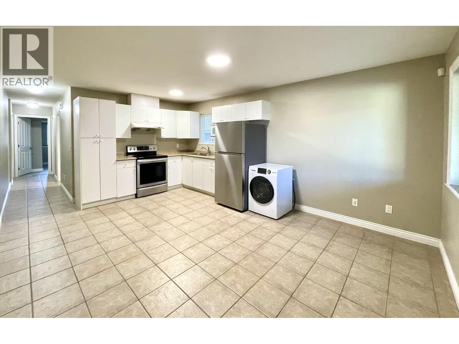A clean, empty living space with a kitchen area and a laundry machine.