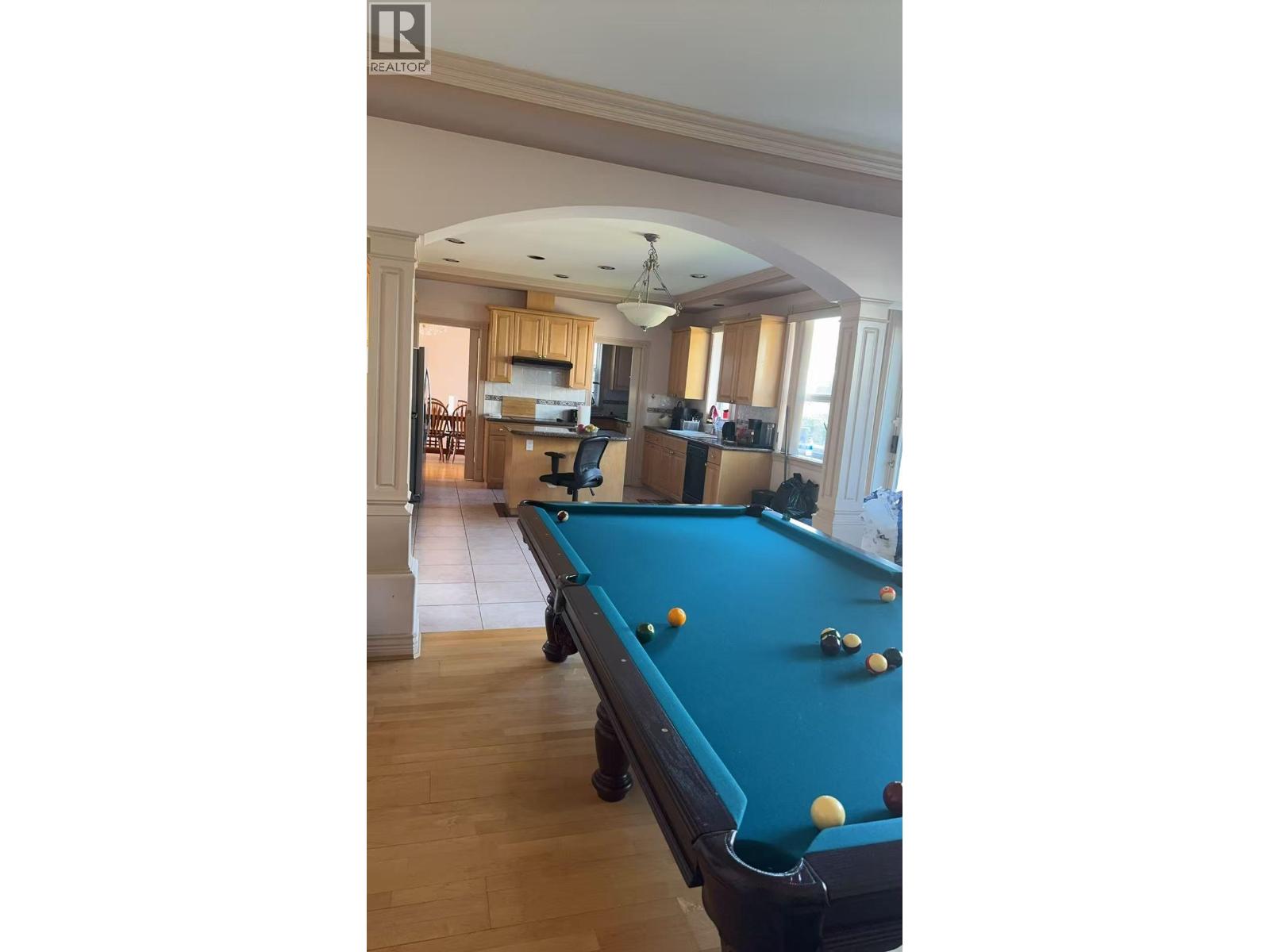 A pool table in a room with a high ceiling and a bar area.