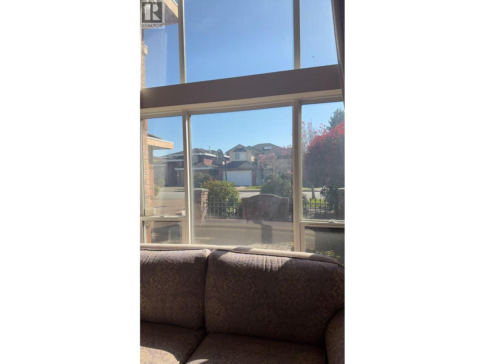 A couch is in front of a window with a view of a house and trees.