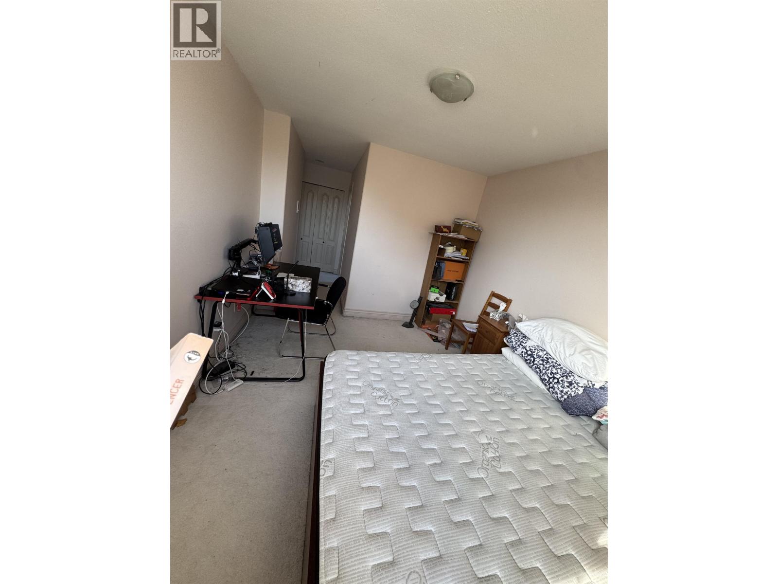 A bedroom with a bed, a desk with a computer, and a bookshelf.