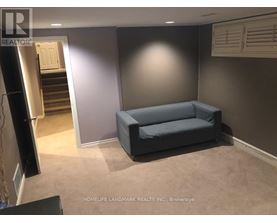 A living room with a grey couch and a staircase in the background.