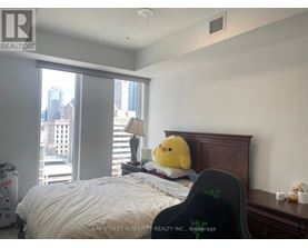 A bedroom with a bed, a yellow duck pillow, and a window overlooking a cityscape.
