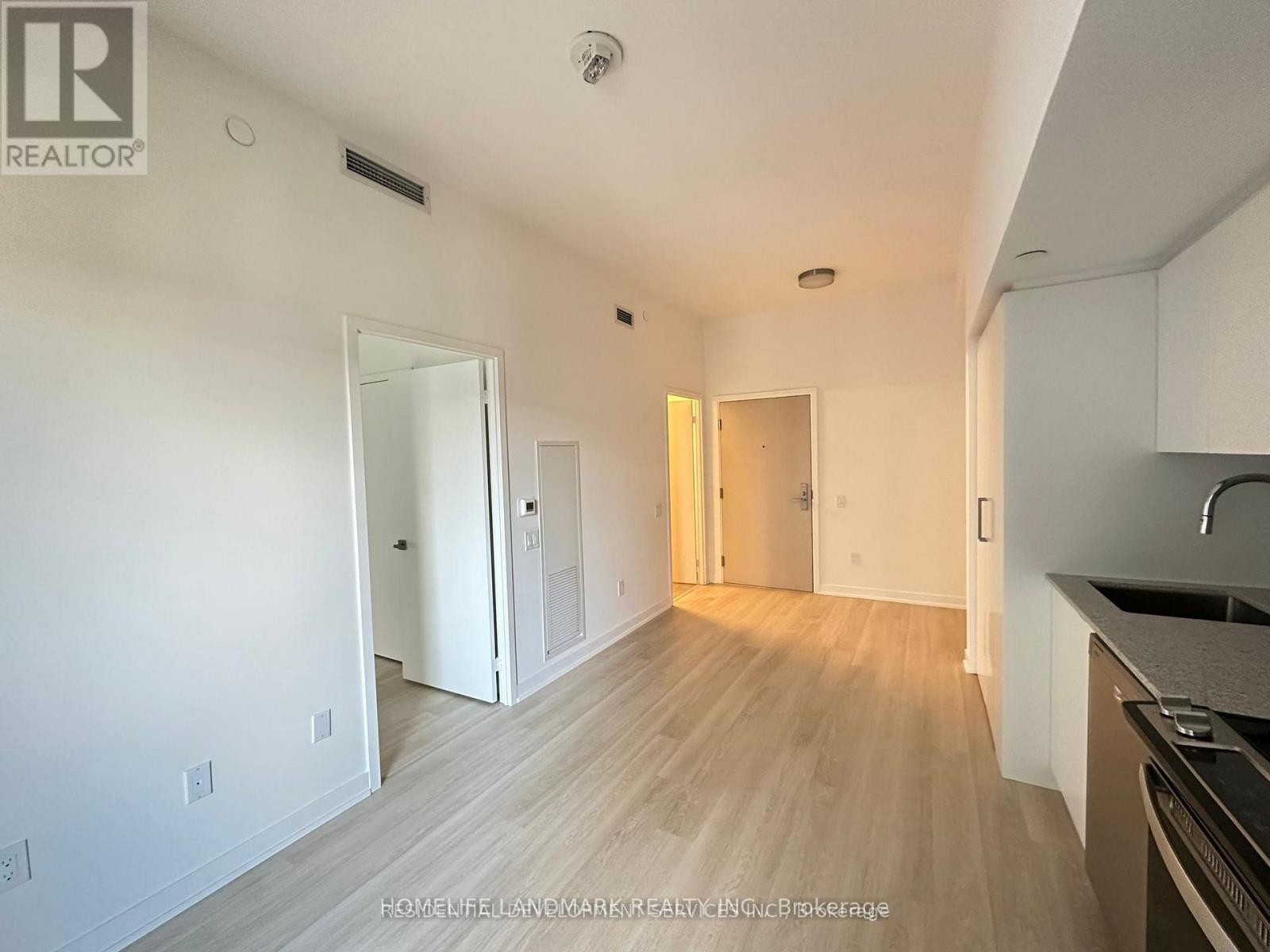 A well-lit, empty room with a kitchen area to the right.