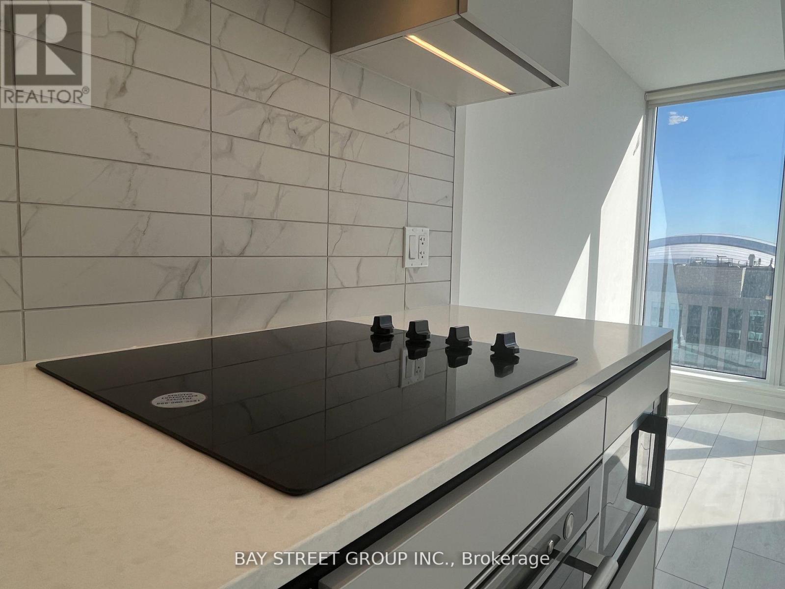 A modern kitchen with a black stove top and a marble backsplash.