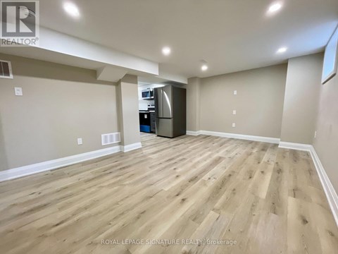A spacious room with wooden flooring and a kitchenette in the corner.