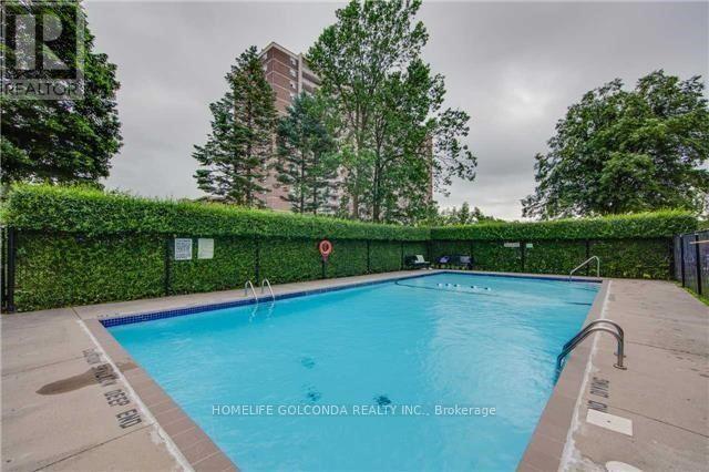 A pool surrounded by a black fence and greenery.