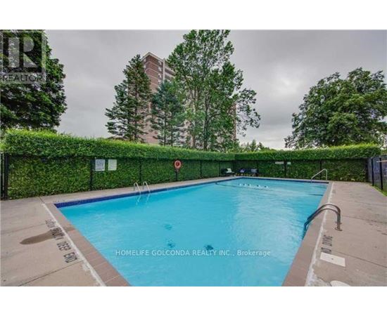 A pool surrounded by a black fence and greenery.