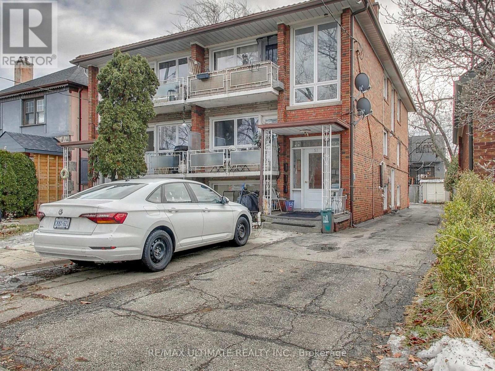 A white car is parked in front of a two-story brick building.