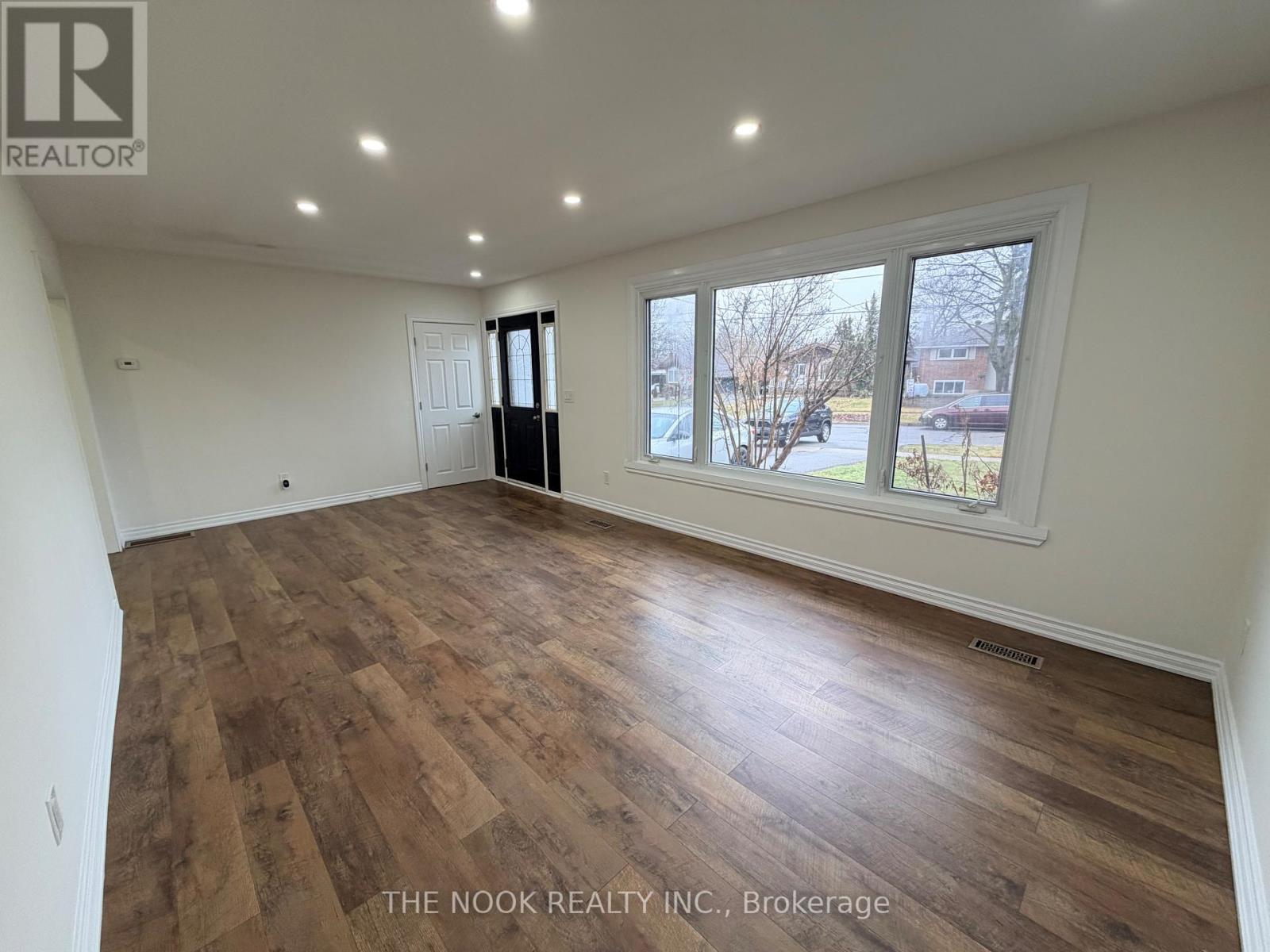 A room with wooden flooring and a large window overlooking a residential area.