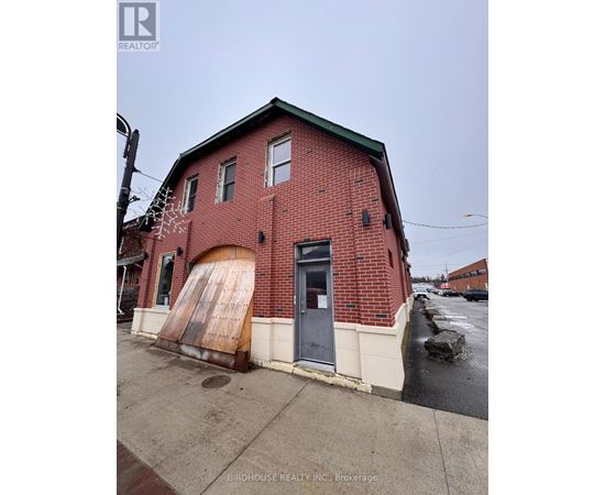 A red brick building with a large door and a sign that says Birdhouse Realty Inc Brokerage.