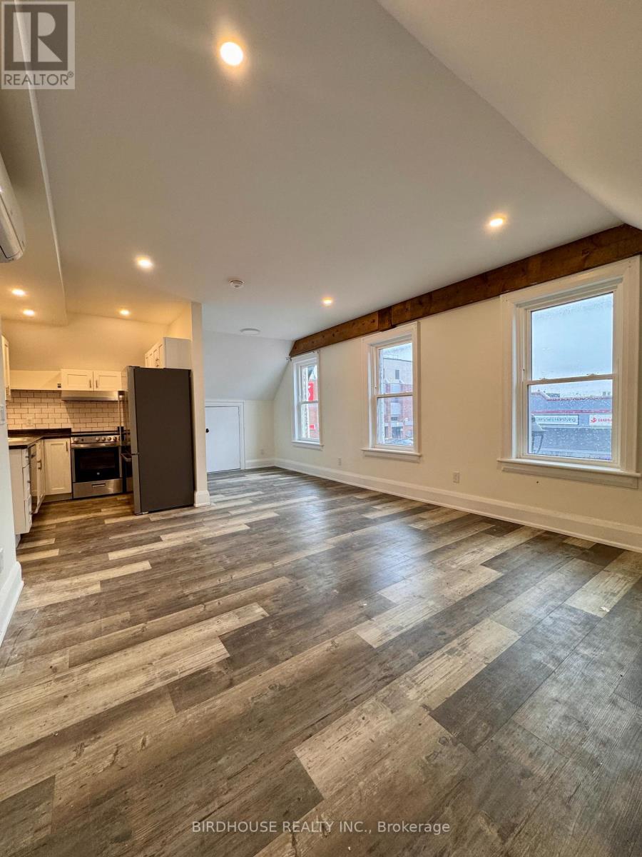 A spacious room with wood flooring and a kitchen area with a refrigerator.