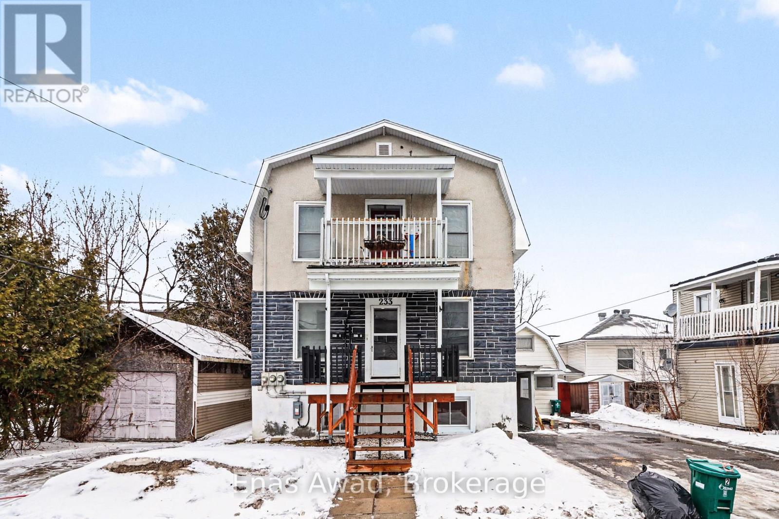 A house with a snow-covered front yard and a green trash can.