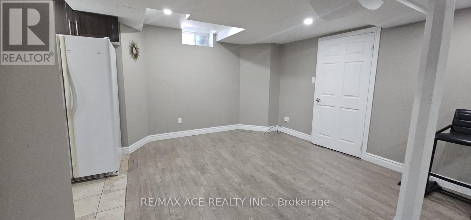 A spacious room with a white door and a fridge in the corner.