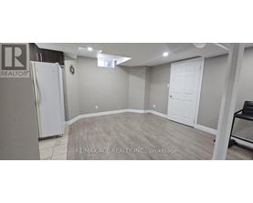 A spacious room with a white door and a fridge in the corner.