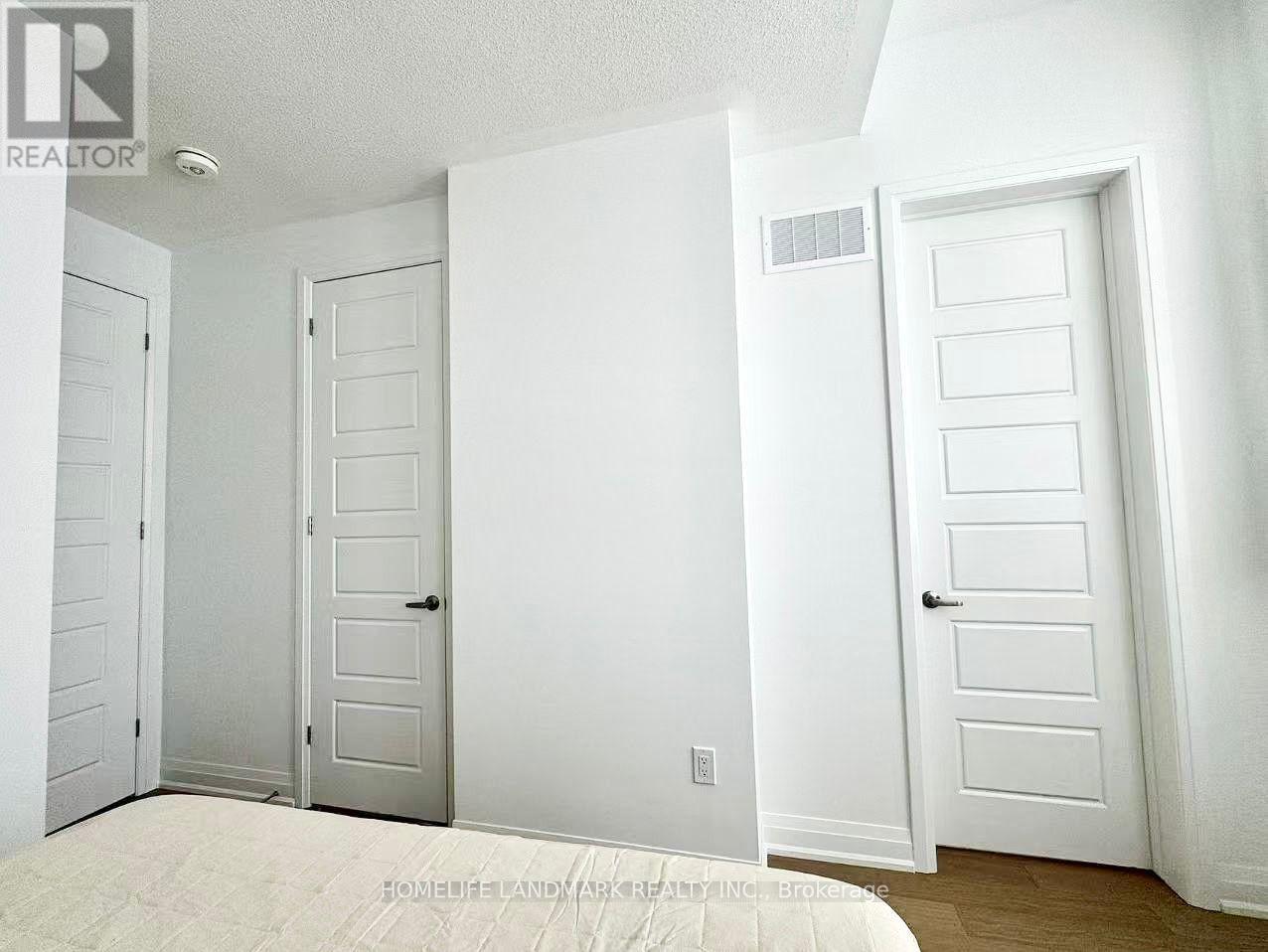 A white bedroom with a bed and three doors.
