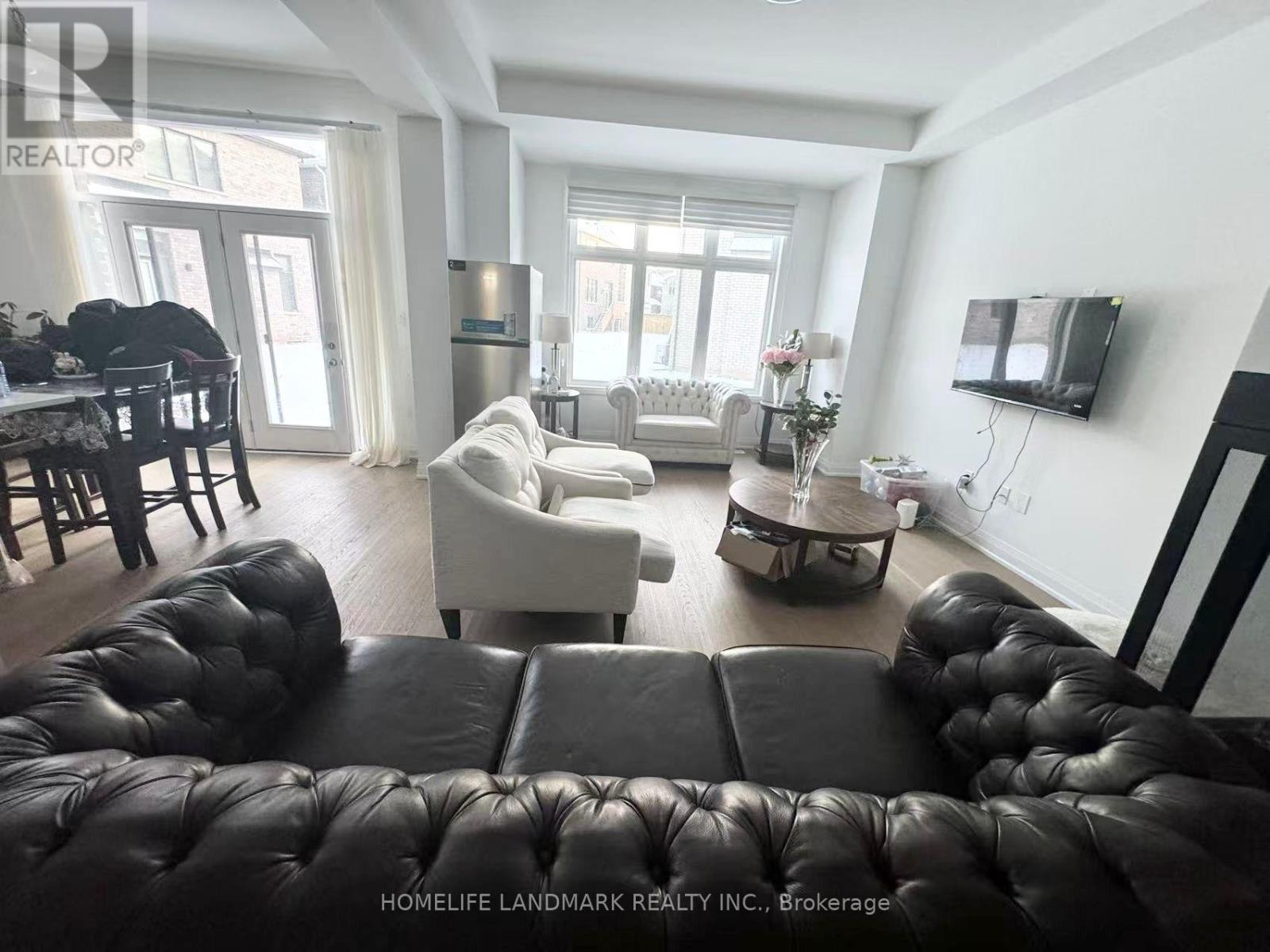 A living room with a black leather couch and a television on the wall.