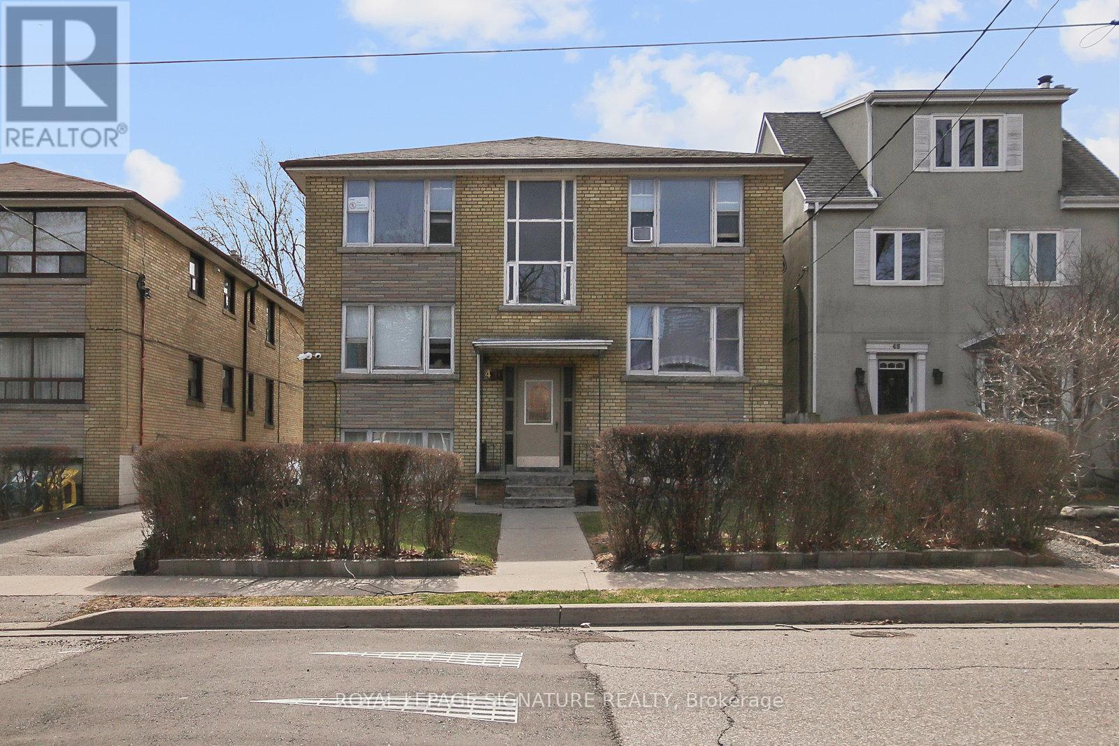 A building with a grey facade and a brown door is surrounded by a hedge.