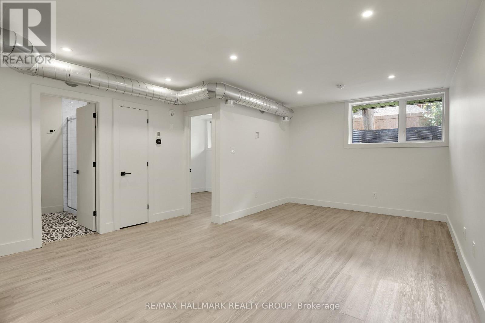 A spacious room with wooden flooring and white walls, with a window on the right side.
