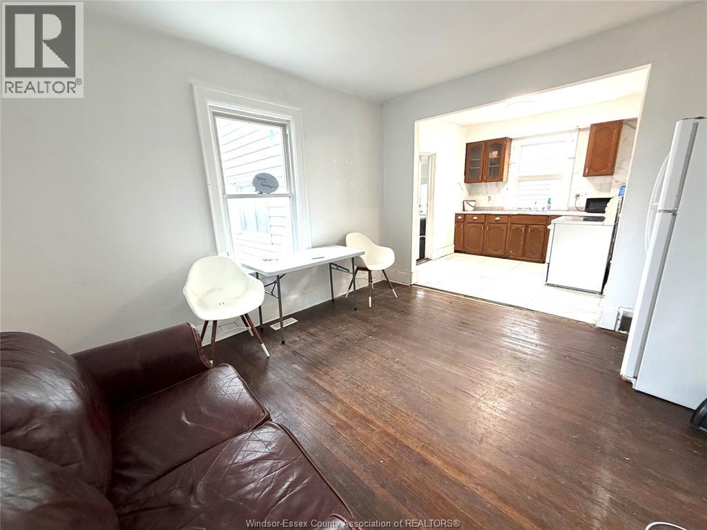 A brown leather couch sits in a living room with a dining area in the background.