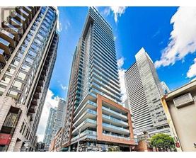 A tall building with a glass facade stands in front of a row of shorter buildings.