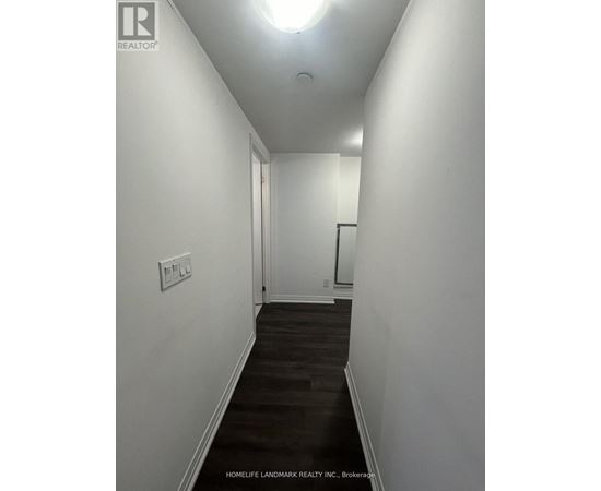 A long hallway with a light on the ceiling and a door at the end.