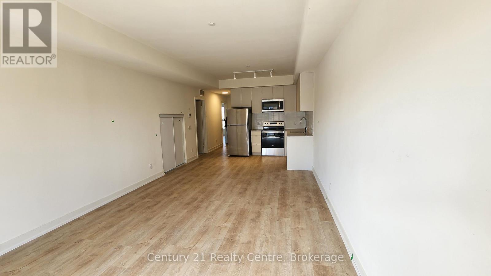 A spacious room with wooden flooring and a kitchenette in the distance.