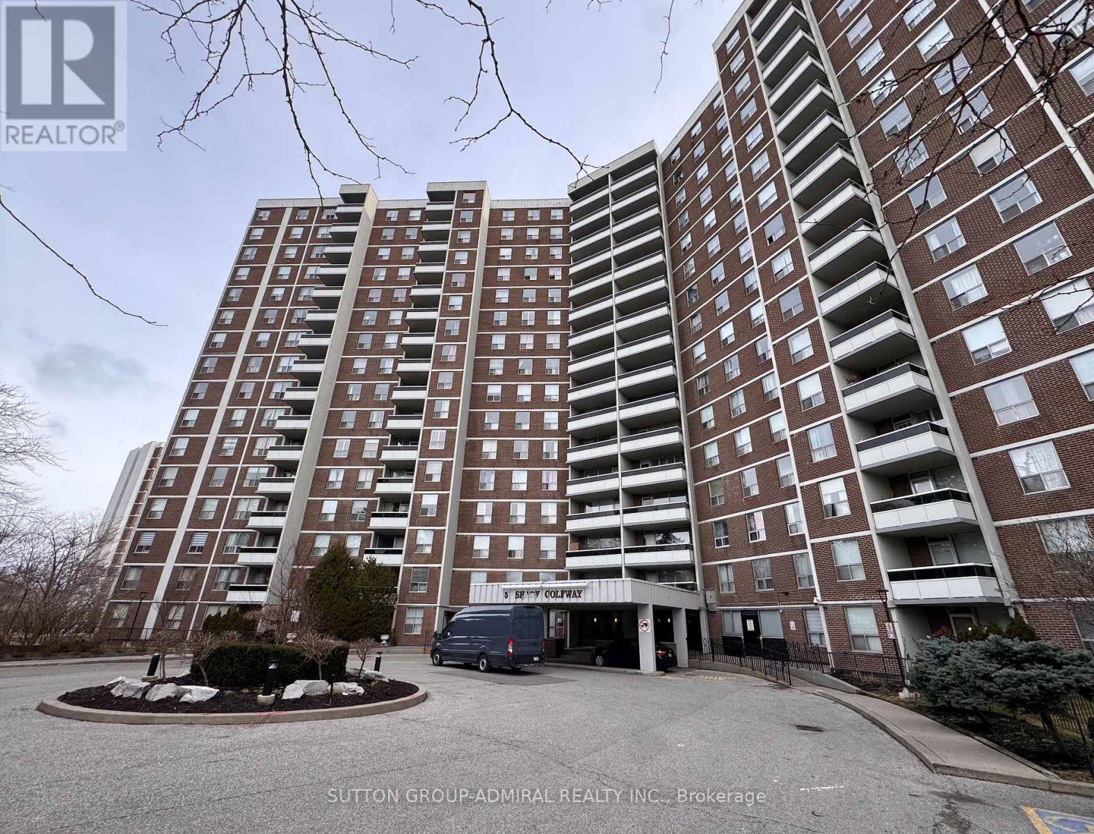 A tall apartment building with a parking lot in front.