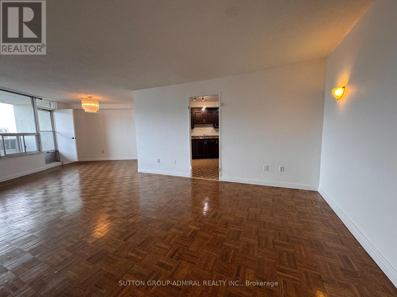 A room with wooden flooring and white walls, with a logo of REALTOR in the top left corner.