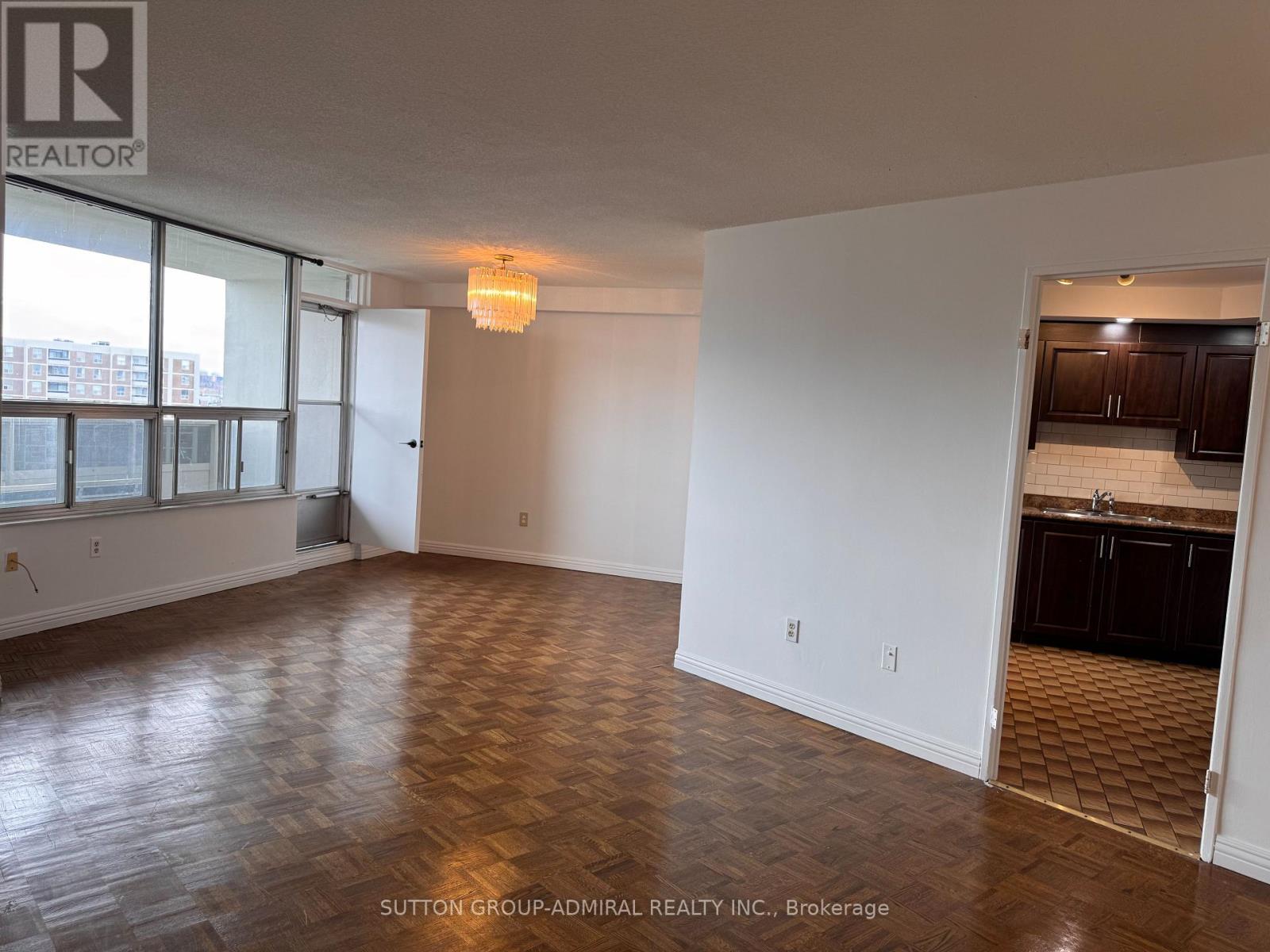 A room with wooden flooring and a kitchen area in the background.