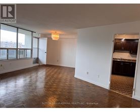 A room with wooden flooring and a kitchen area in the background.