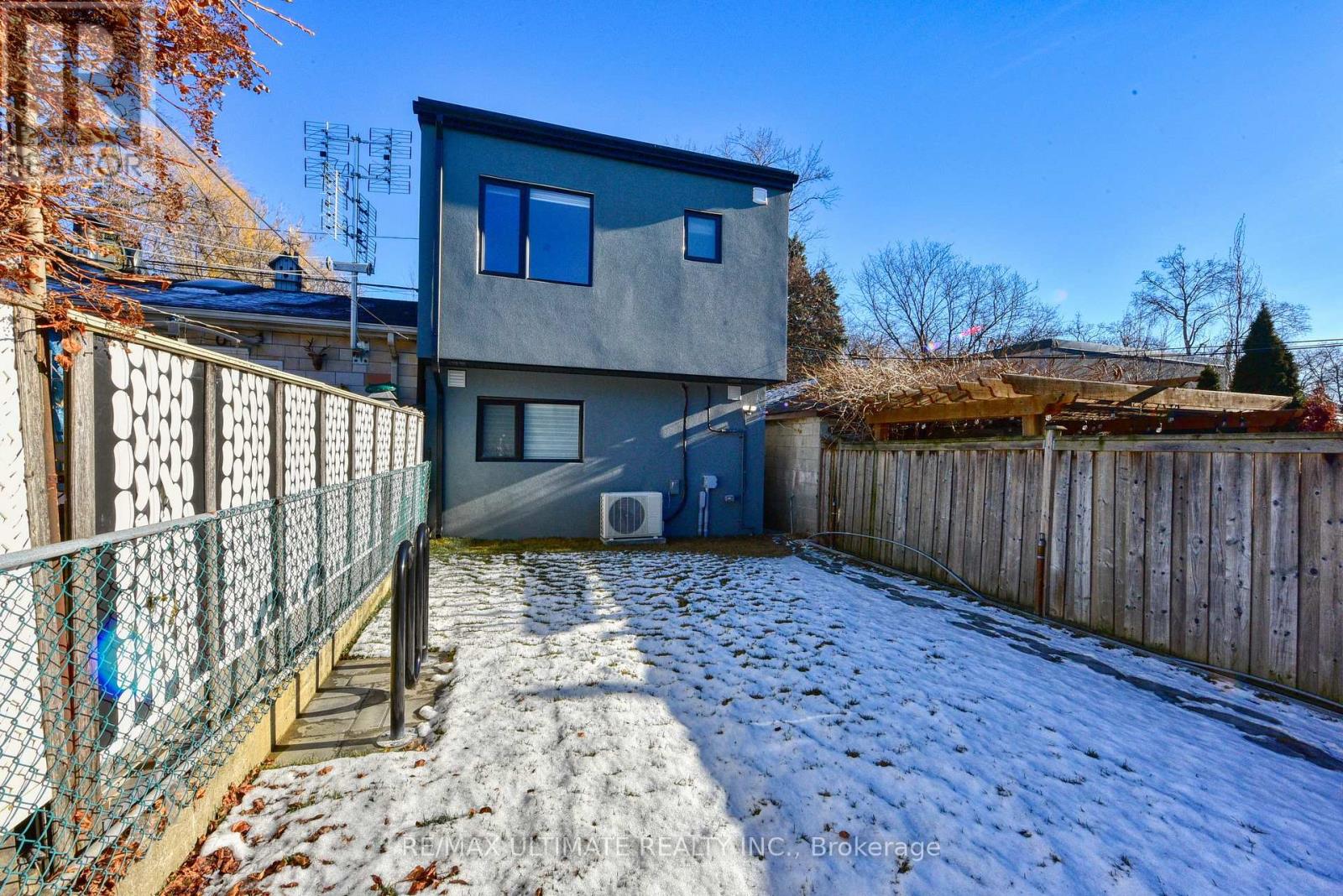 A grey house with a fence and snow on the ground.