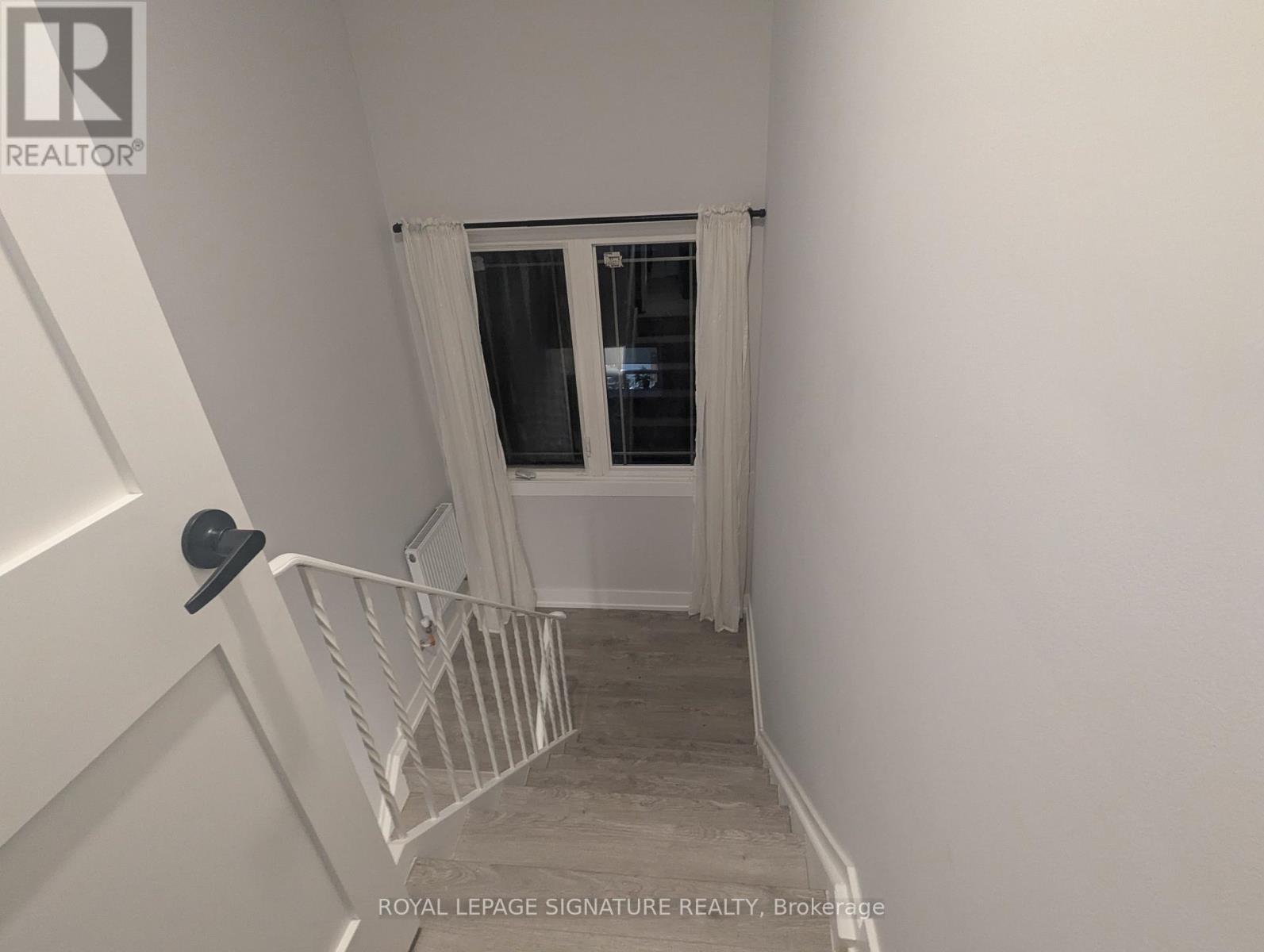 A white hallway with a black door knob and a window with white curtains.