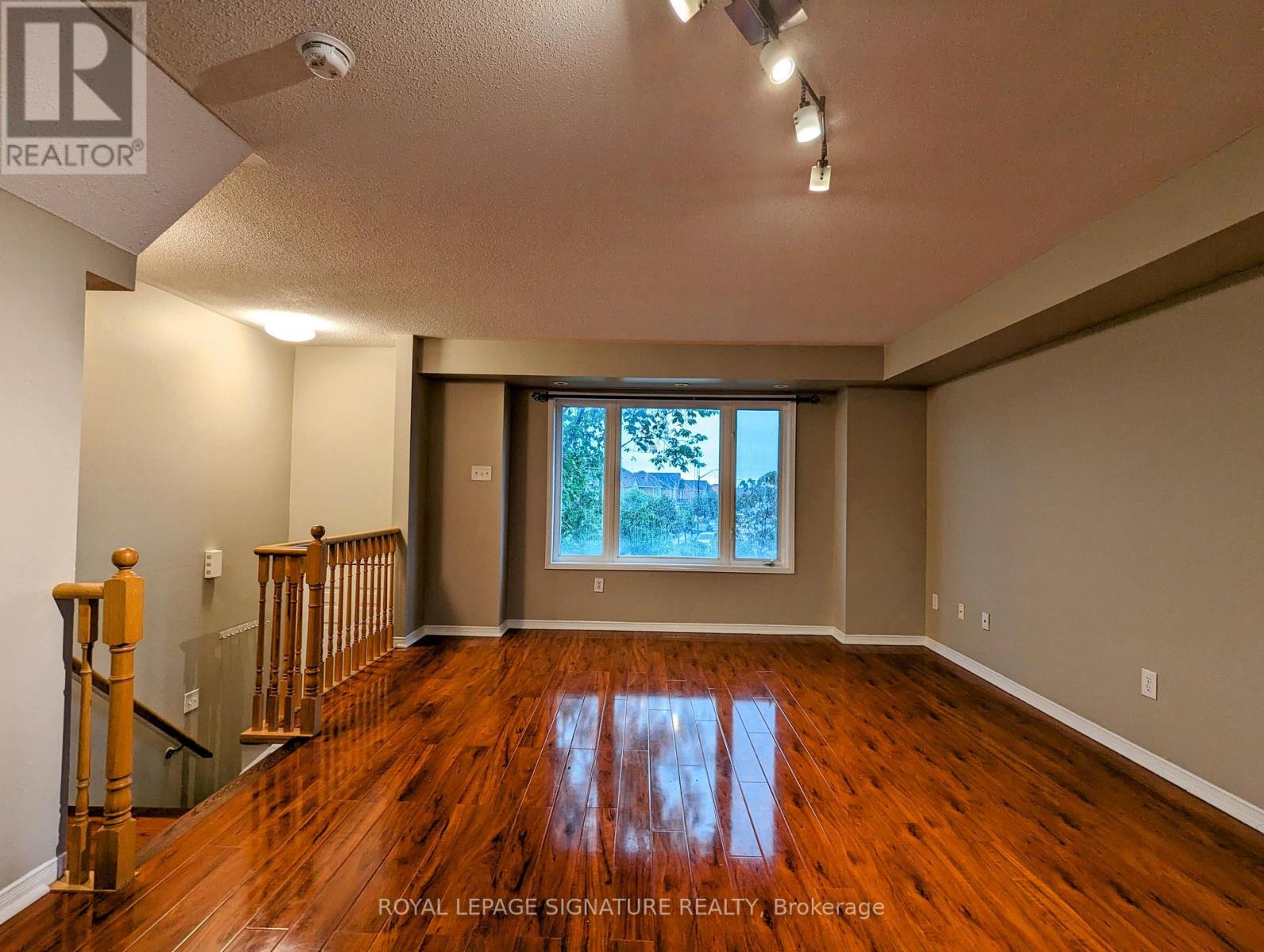 A spacious room with wooden floors and a staircase on the left side.