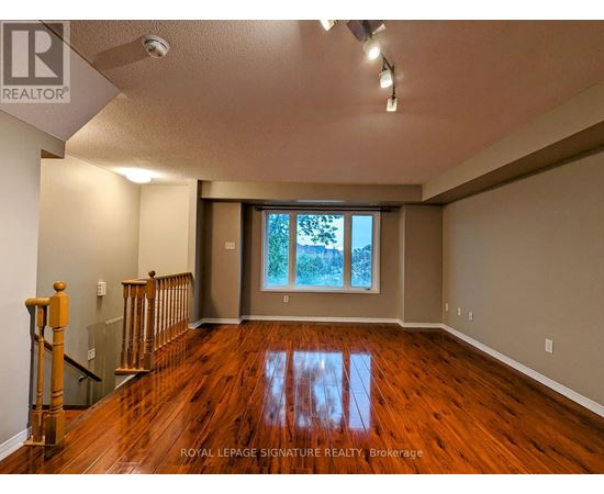 A spacious room with wooden floors and a staircase on the left side.