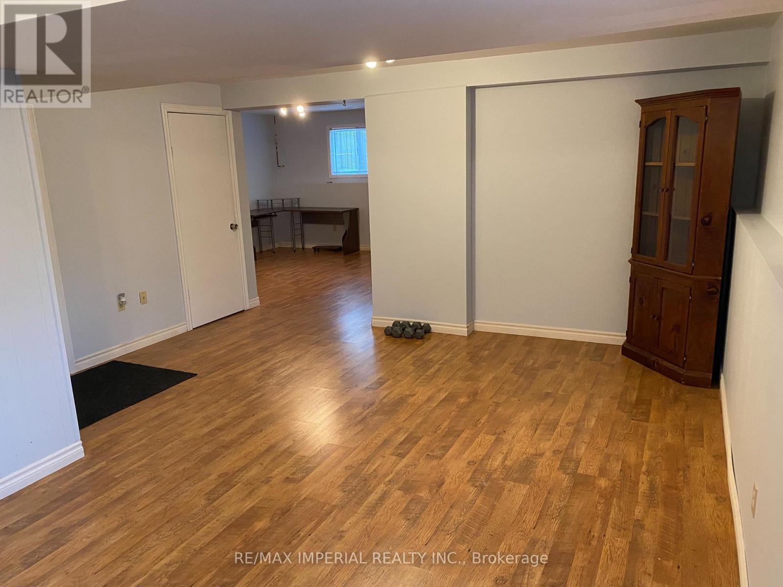 A room with wooden flooring and white walls, with a cabinet and a door visible.