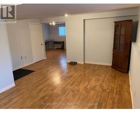 A room with wooden flooring and white walls, with a cabinet and a door visible.