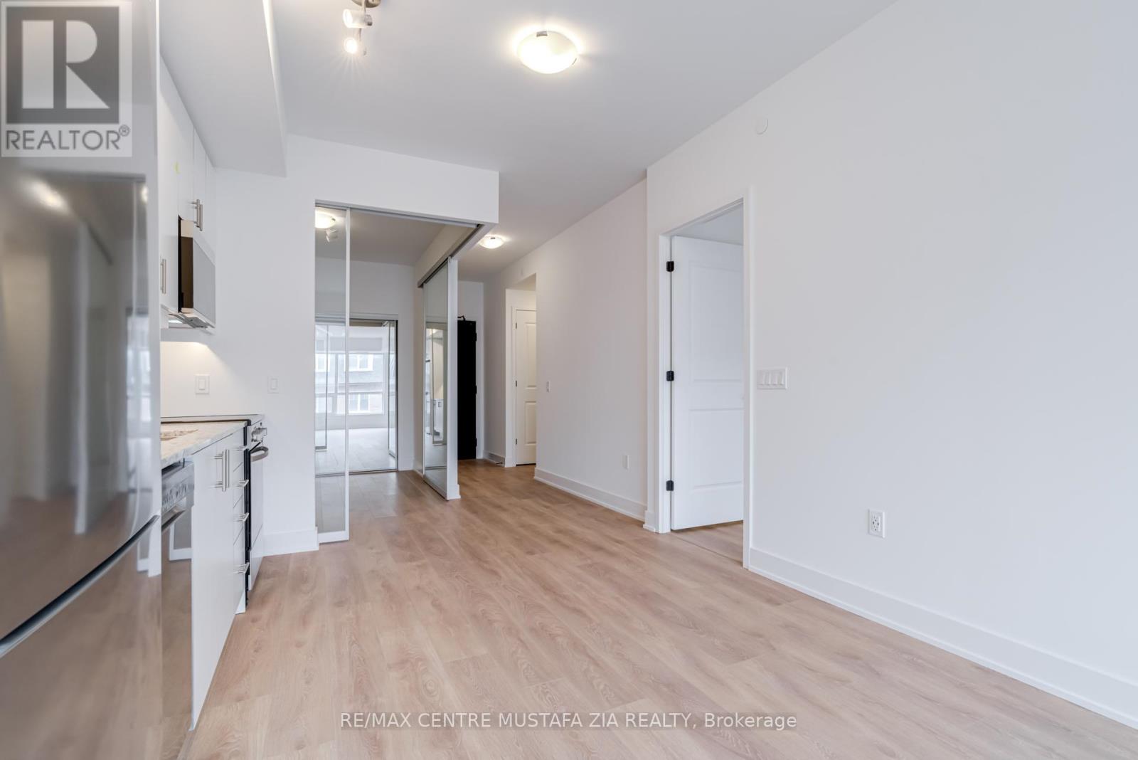 A spacious, empty apartment with wood flooring and white walls.