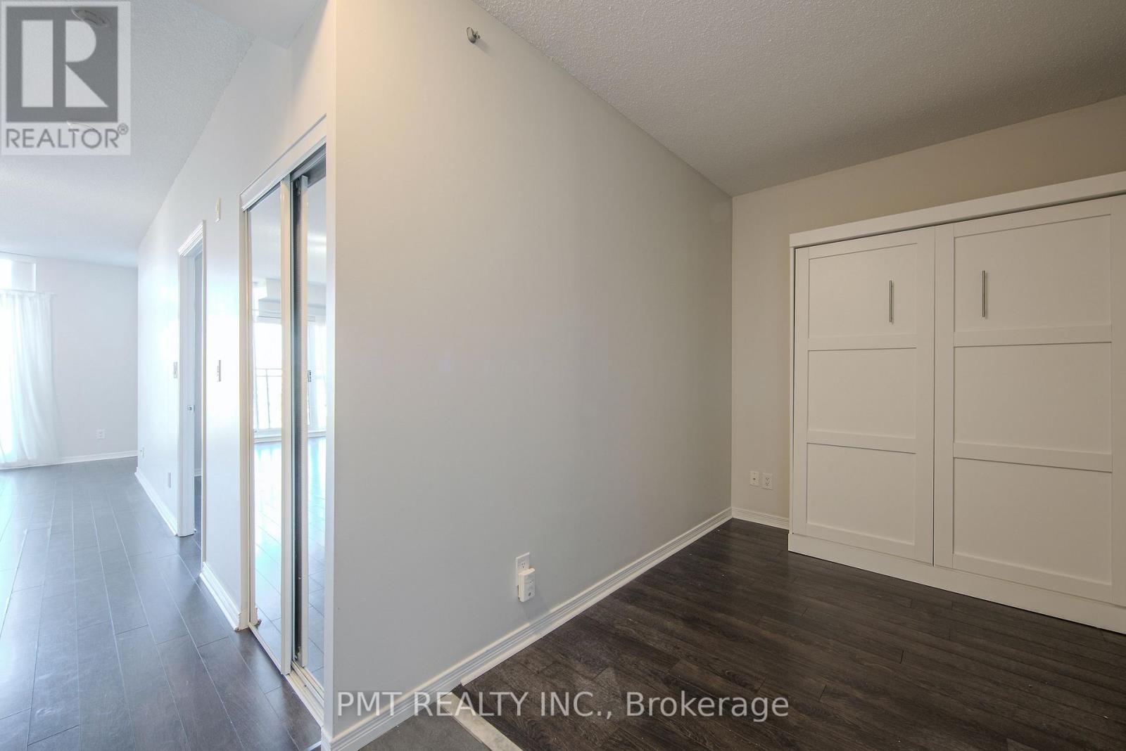 A room with white walls and wooden floors, with a door on the left and a cabinet on the right.