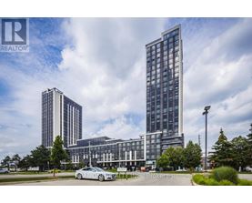 A tall building with a glass facade stands in front of a smaller building and trees.