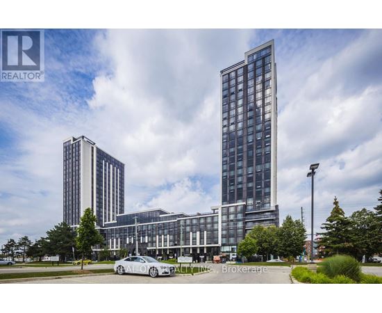 A tall building with a glass facade stands in front of a smaller building and trees.