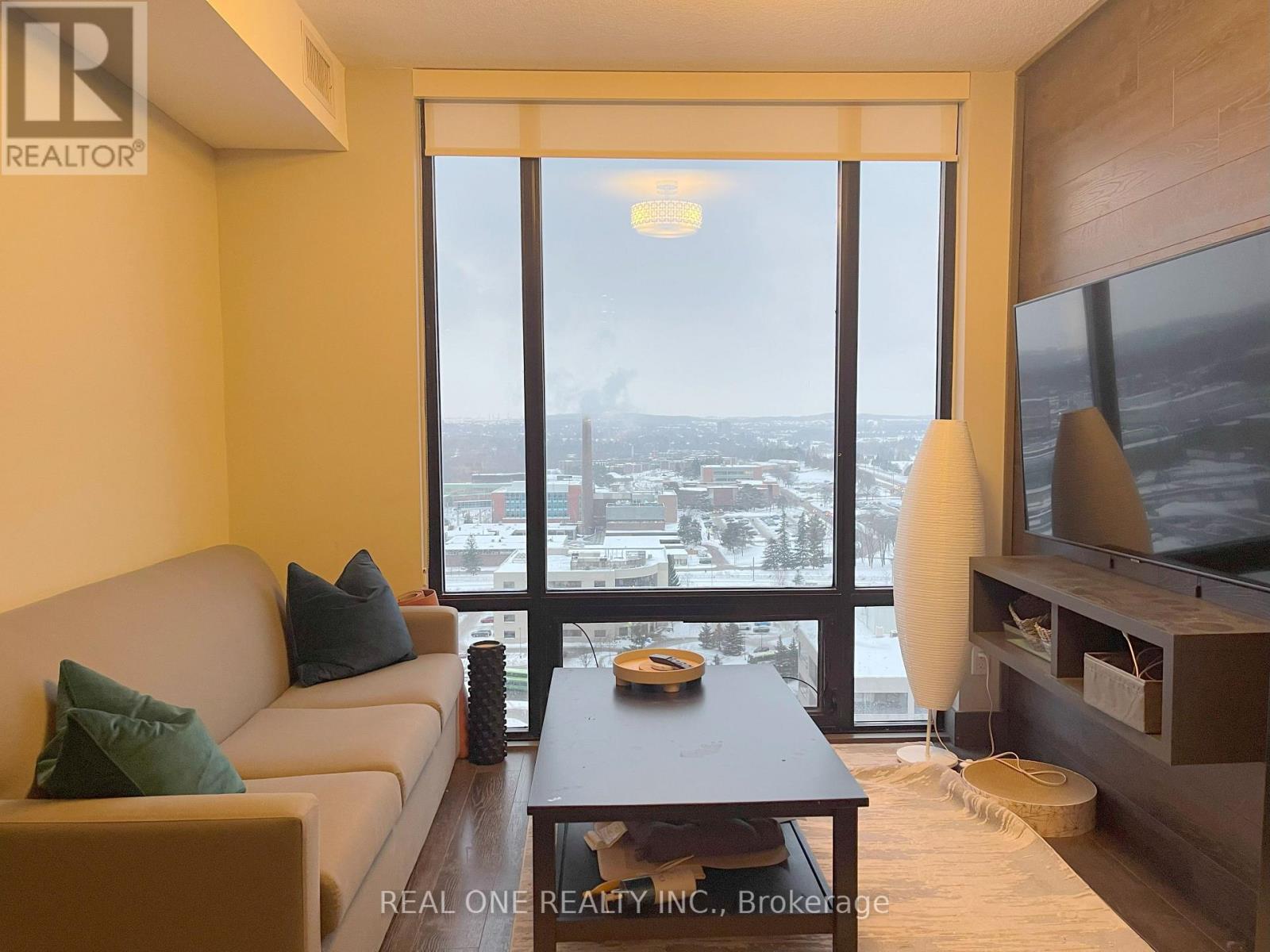 A living room with a couch, a coffee table, and a large window overlooking a cityscape.