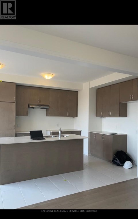A modern kitchen with brown cabinets and a laptop on the counter.