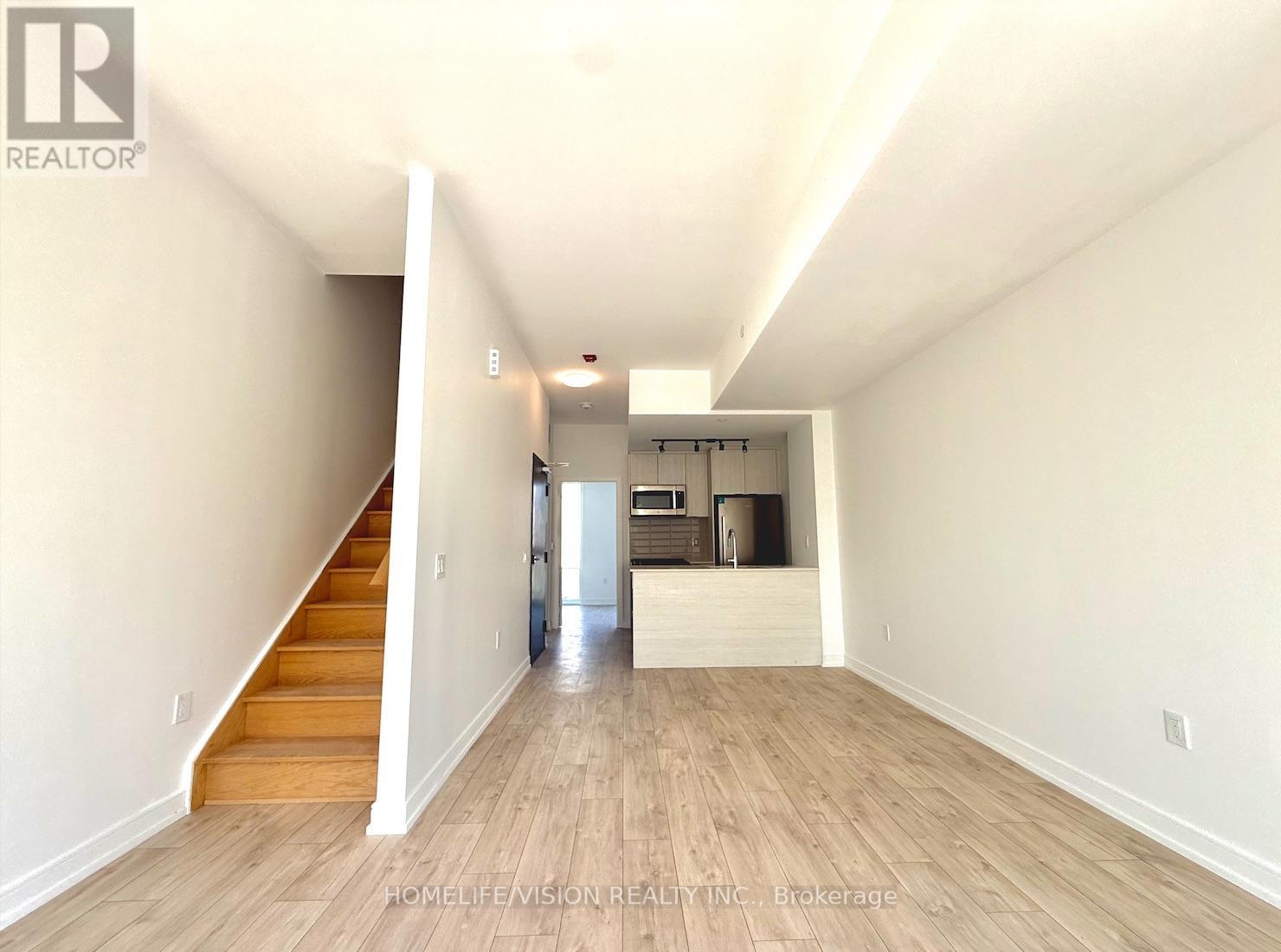 A spacious room with wooden floors and a staircase leading to another level.