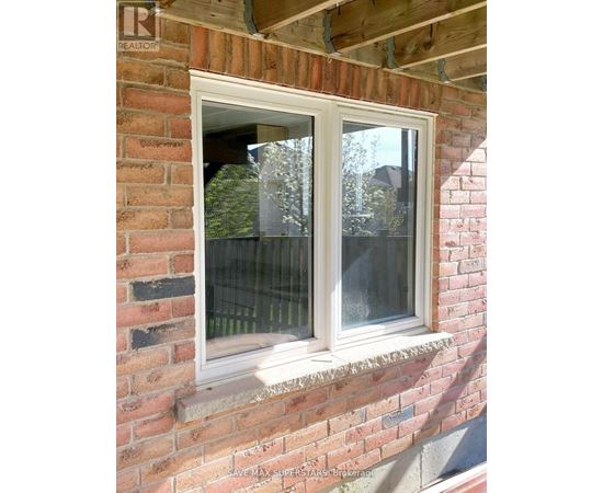 A window on a brick wall with a view of a fence and trees.
