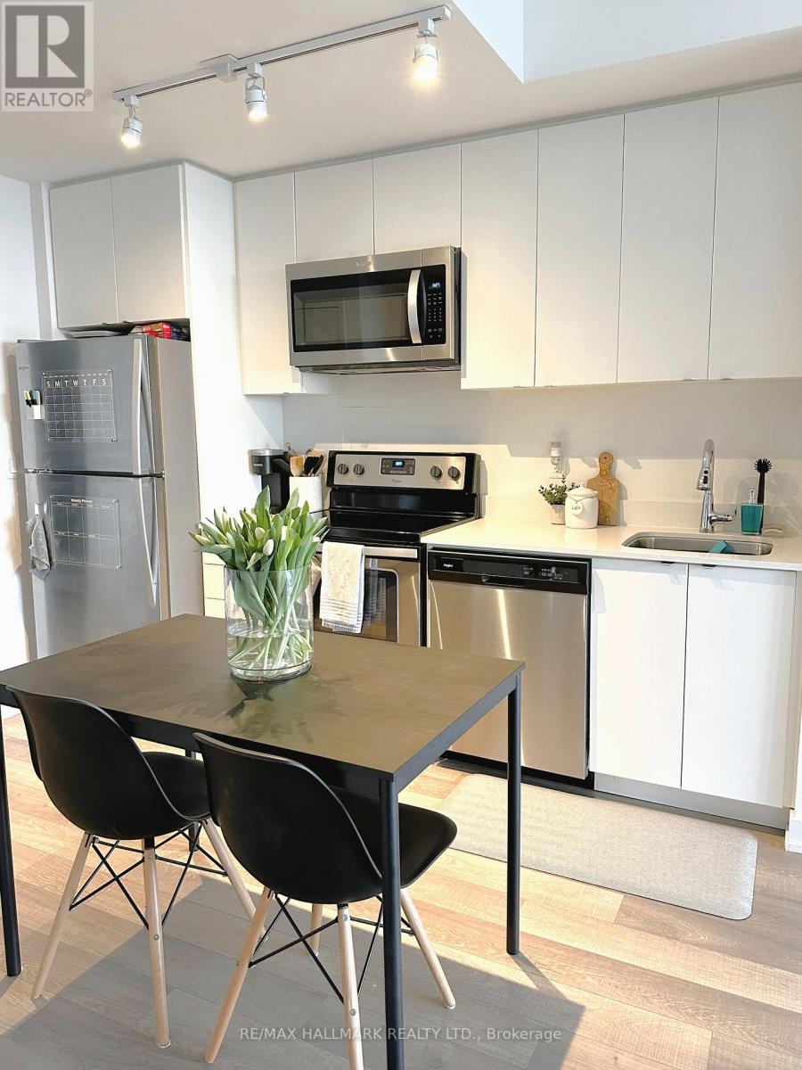 A kitchen with a table and chairs in the foreground and a refrigerator, microwave, oven, and sink in the background.