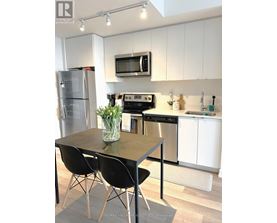 A kitchen with a table and chairs in the foreground and a refrigerator, microwave, oven, and sink in the background.